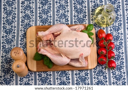 Still life of a raw chicken on a board with tomatoes, oil, salt shaker and pepper grinder.