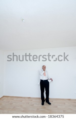 A metaphorical image of a broke businessman standing in an empty room of a new house.