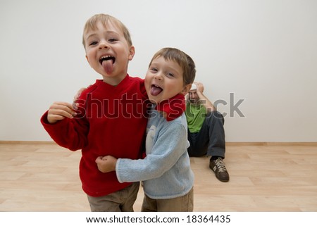 Portrait of two noisy children being naughty, with adult in background sat on floor covering his ears.