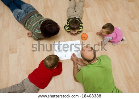 A family comprising parents and their 3 kids lying on the floor and checking the design of their new house on the paper.