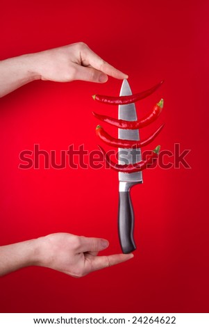 Chili peppers on a large knife with fingers holding it.