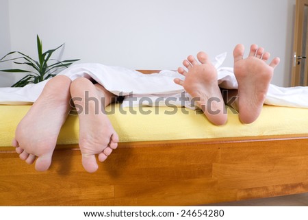 Two pairs of feet under sheets hanging over the edge of a bed.
