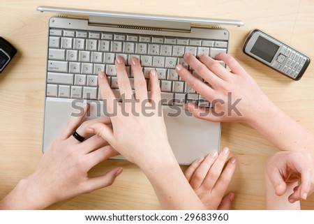 A laptop computer with hands typing and a cell phone.