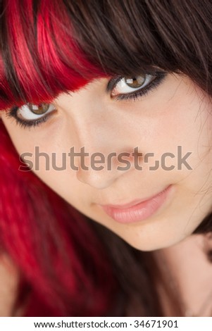Closeup on a serious young woman with partially dyed red brunette hair and large brown eyes.