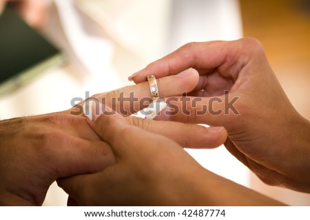 Closeup of bride placing wedding ring on finger of groom.
