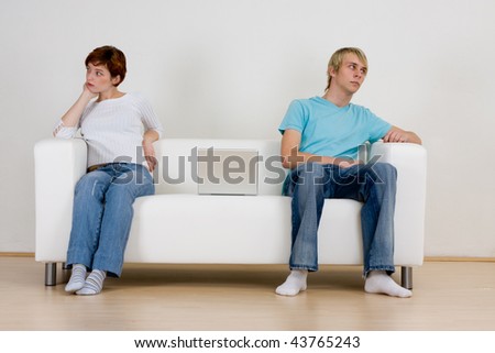 A young teen couple sitting on opposite ends of a sofa, not talking and ignoring each other.  Theme: non-communication.