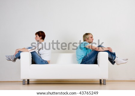 Couple sitting back to back on a sofa, ignoring each other after a fight.