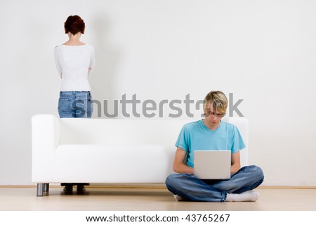 Young couple in room with man on laptop and woman standing behind couch.