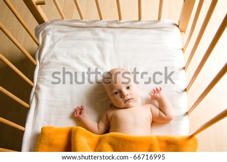 Overhead view of cute baby boy lying under blankets in wooden crib or cot.