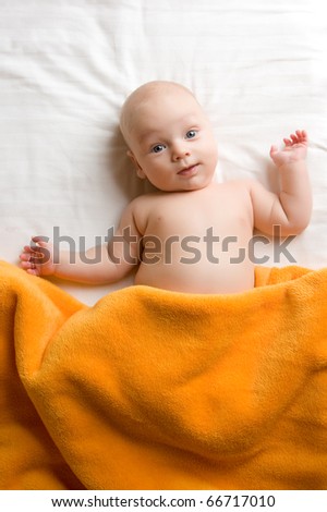 Overhead view of cute baby boy lying under blanket in bed.