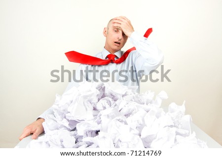 A stressed man holding his head behind a pile of papers.
