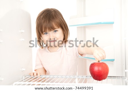 A young girl reaching for a large apple in a refrigerator.