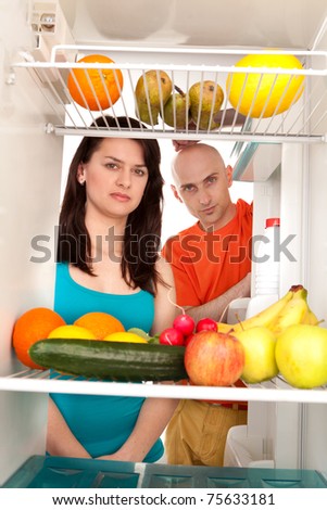 Young couple eating and looking at healthy fruit and vegetable in modern refrigerator, isolated on white background.
