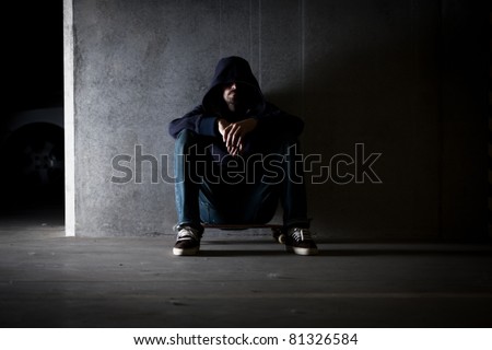 Hooded man sitting against wall.