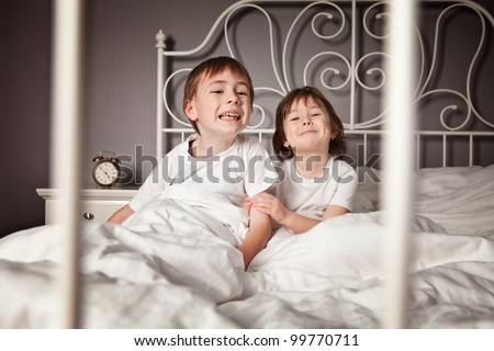Brother and Sister in their parents bed pulling funny faces.