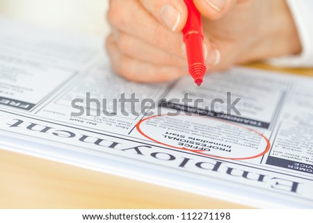 A hand with a pen circling a job in the paper (focus on pen nib and ad)