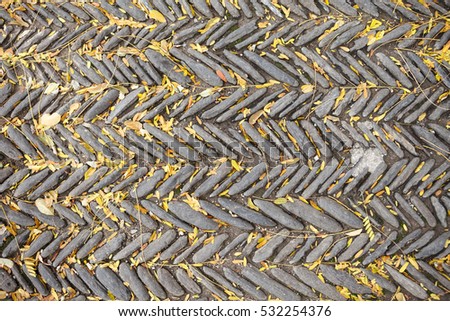 The texture of the old herringbone pavement of cobblestones with moss and autumn yellow leaves between the stones in the monastery courtyard in Spain. View above