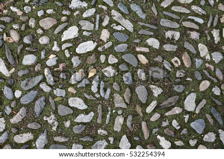 The texture of the old pavement of randomly laid cobblestones with moss between the stones in the monastery courtyard in Spain