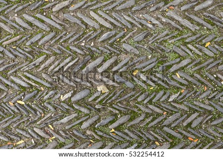 The texture of the old herringbone pavement of cobblestones with moss between the stones in the monastery courtyard in Spain. View above