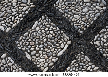 The texture of the old pavement of randomly laid cobblestones with with an ornament in the form of a lattice of the black stones in the monastery courtyard in Spain. View above