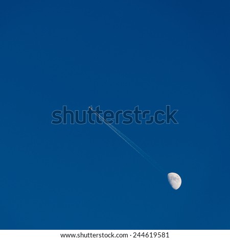 Moon and passenger airplane in blue sky, large trail of the plane