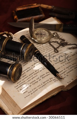 Still-life - old things placed on an open ancient cyrillic book. Objects include: a Montblanc pen, a watch, a field-glasses, a knife and other.