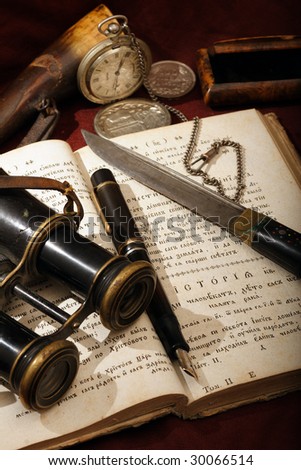 Old things placed on an open ancient cyrillic book. Objects include: a Montblanc pen, a watch, a field-glasses, a knife and other.