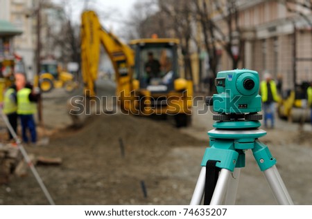 Theodolite, excavator and workers at road construction site