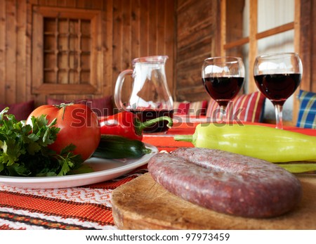 Wine, sausage and vegetables on table, traditional Bulgarian table setup with fresh food and glasses of red wine