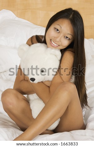 Asian woman in early 20\'s setting in bed hugging a teddy bear