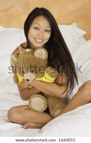 Asian woman in early 20's sitting in bed hugging a teddy bear