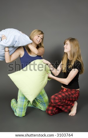 Teenage sisters having a pillow fight on a gray background