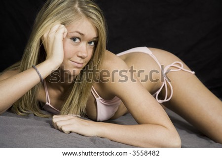 Caucasian teenager wearing a Brazilian cut bikini posing in a studio on a black background