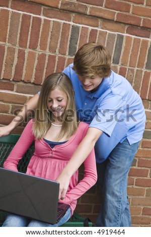 Young teenagers a boy and a girl working on a laptop computer outside a school.
