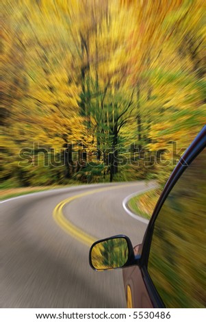 Automobile driving down a country road with the autumn colors and a blured affect
