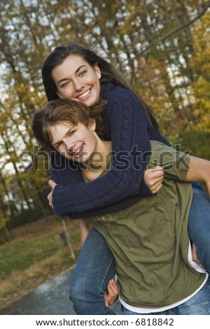 Caucasian teens one male and one females horsing around in a park riding piggy back