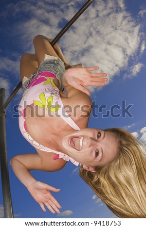 Beautiful Caucasian female teenage hanging upside down on outdoor gym bar and wearing a swimsuit.
