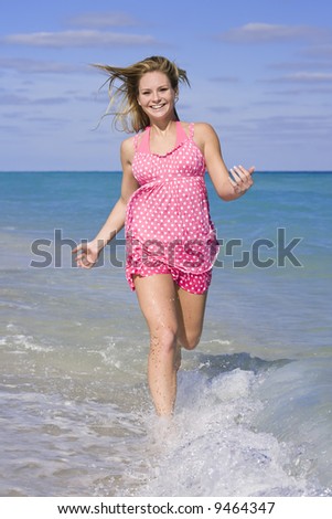 Beautiful Caucasian female teenage running through to surf wearing a colorful sundress.