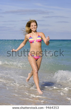 Beautiful Caucasian female teenage running through to surf wearing a colorful bikini.