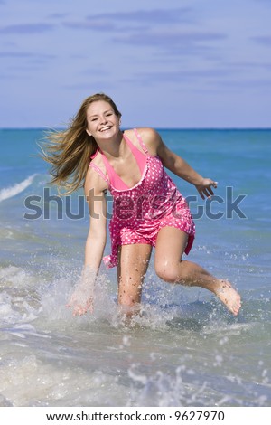 Beautiful Caucasian female teenage running through to surf wearing a colorful  sundress and bikini.