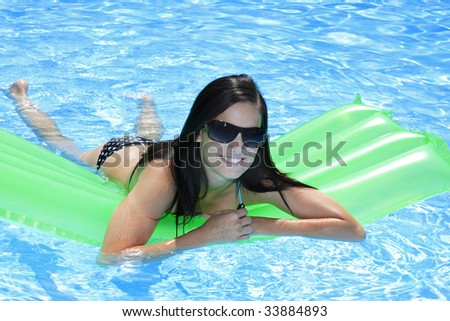 Attractive slim and tanned young lady lying on inflatable sunbed on sunny swimming pool on vacation or holiday