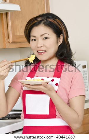 Beautiful Asian woman eating eggs with chop sticks in the kitchen