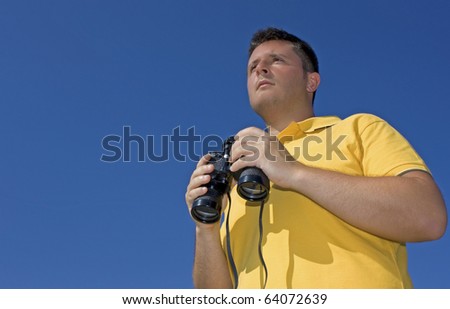 A young man with with binoculars in his hands against blue vivid sky. Young man with binoculars