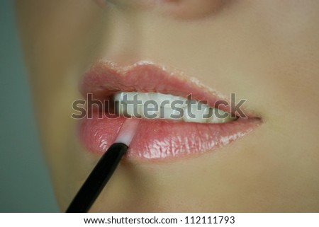 Woman make her lips with lip gloss