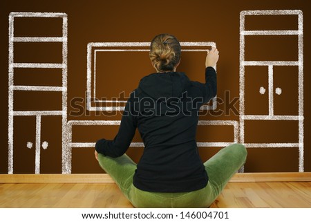 woman is sitting on an empty floor in an empty apartment, and draws on the wall, furniture, cabinets, and TV.