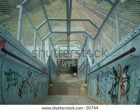 Graffiti covered railway bridge stairway, enclosed by a metal cage.