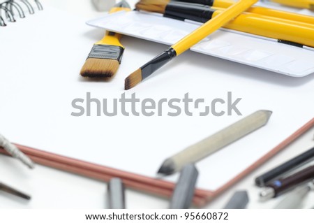 Professional drawing accessories - pens, pencils, brushes and nibs - artists design equipment scattered on sketchbook.