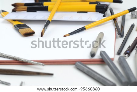 Professional drawing accessories - pens, pencils, brushes and nibs - artists design equipment scattered on sketchbook.