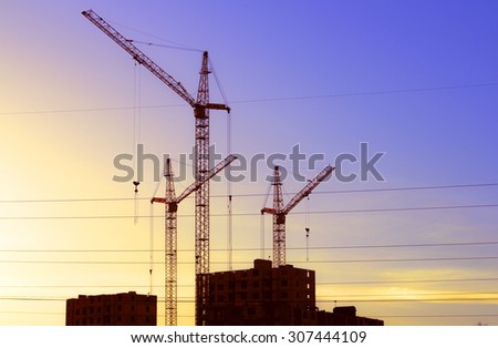 Construction cranes and new buildings silhouette against the backdrop of the sunset sky
