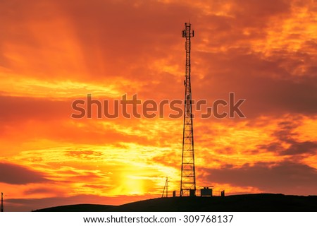 Telecommunications tower black silhouette against a fiery sunset sky